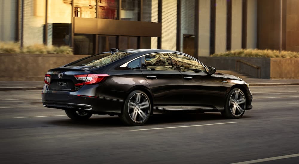 A black 2021 Honda Accord Hybrid is driving on a city street.