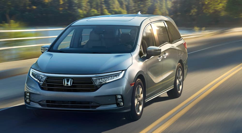 A silver 2021 Honda Odyssey is driving past a pond after winning the 2021 Honda Odyssey vs 2021 Toyota Sienna comparison.