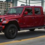 A red 2021 Jeep Gladiator is driving on a city bridge.