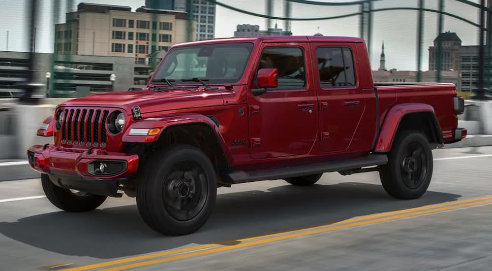A red 2021 Jeep Gladiator is driving on a city bridge.