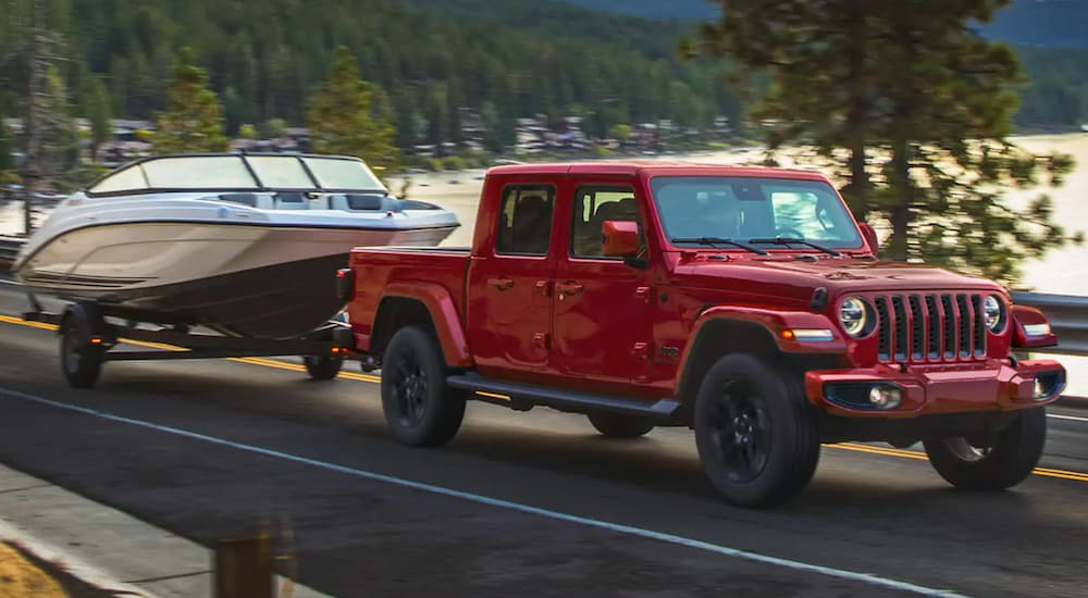 A red 2021 Jeep Gladiator is towing a boat past a lake.