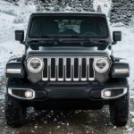 A black 2021 Jeep Wrangler is off-roading on a snowy trail.