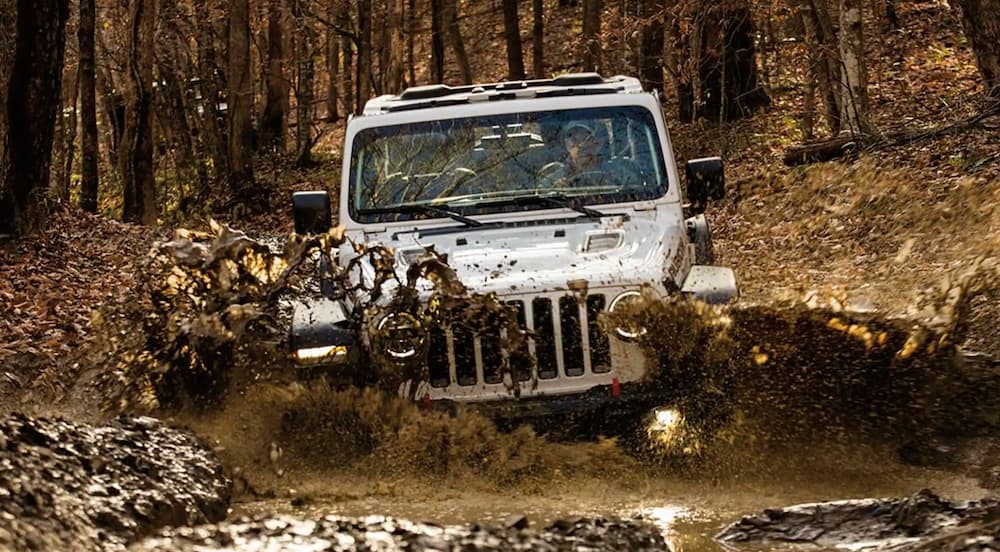 A white 2021 Jeep Wrangler is shown from the front off-roading in the mud.