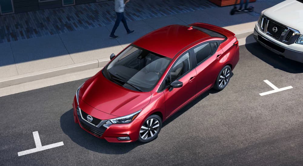 A red 2021 Nissan Versa is backing into a parking spot on a city street.