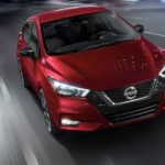 A red 2021 Nissan Versa is driving on a wide city street at night.