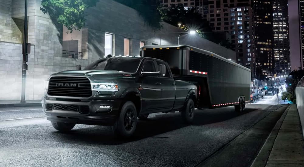 A black 2021 Ram 2500 is towing a trailer on a city street at night.