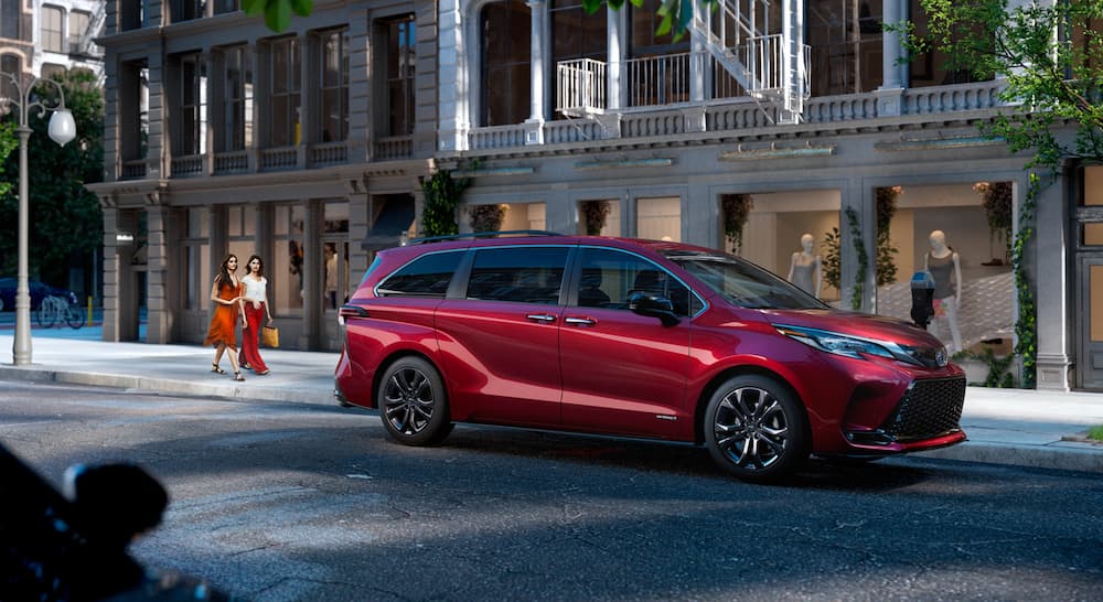 A red 2021 Toyota Sienna is parked on a city street at dusk.