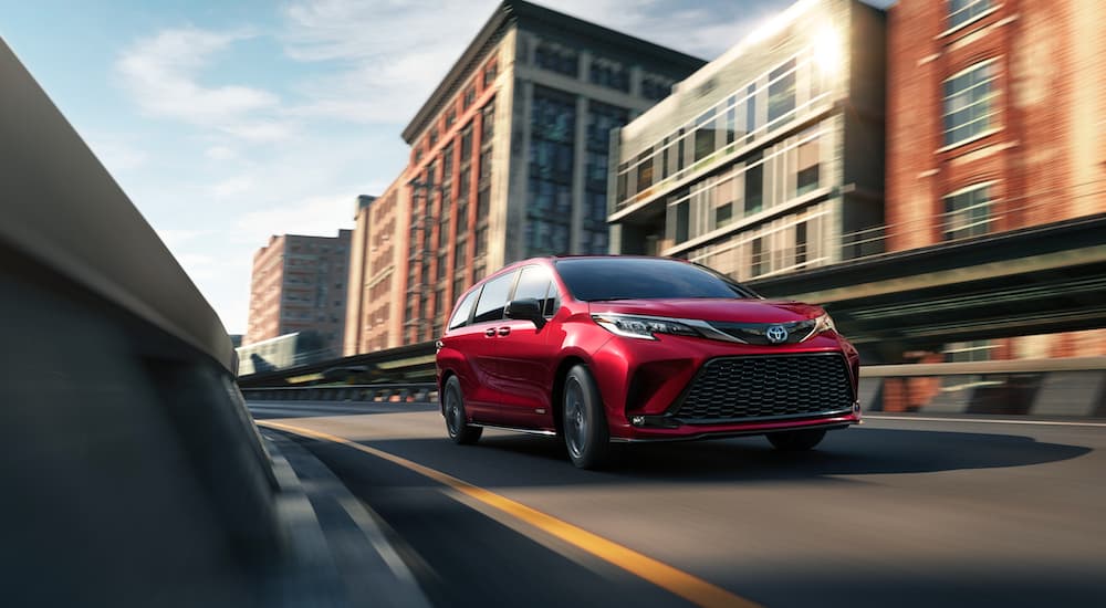 A red 2021 Toyota Sienna is driving on a one lane road in a city.