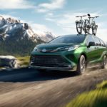 A green 2021 Toyota Sienna with bikes on the roof is driving on a dirt road past mountains.