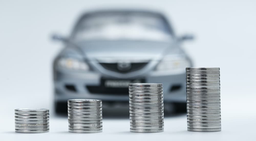 A close up shows increasing stacks of quarters with a blurred car in the background.