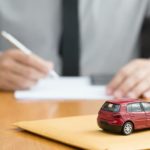 A close up shows a red toy car and a man filling out paperwork for a buy here pay here car loan.
