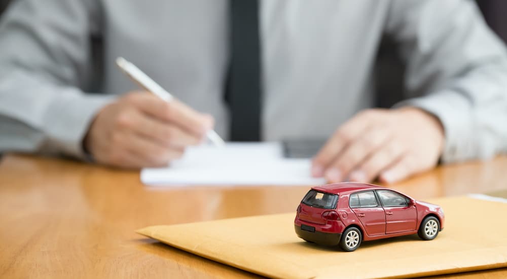 A close up shows a red toy car and a man filling out paperwork for a buy here pay here car loan.