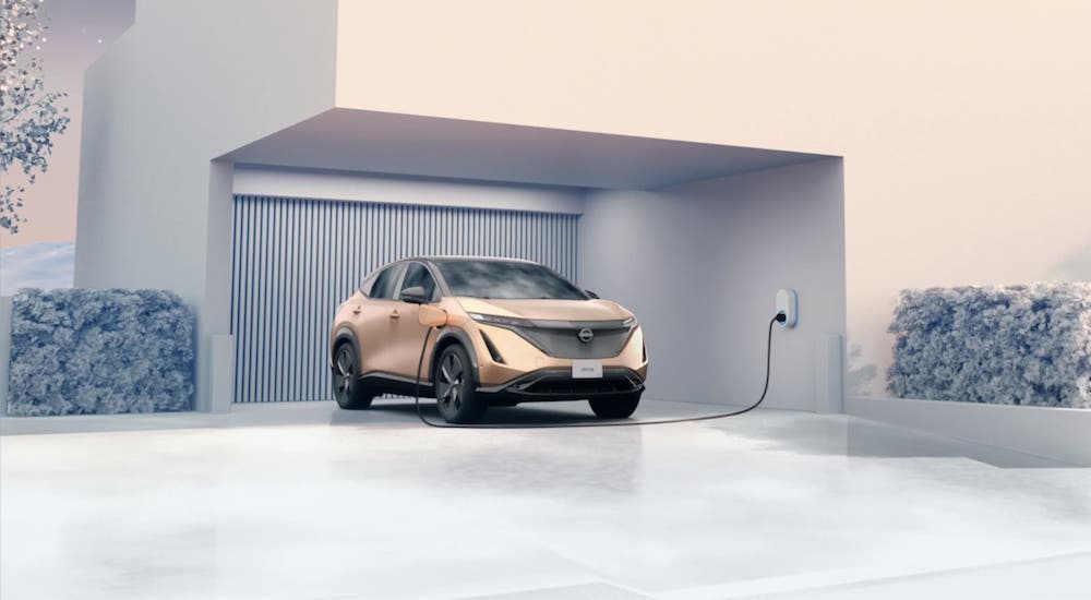 A gold 2021 Nissan Ariya is plugged into a modern house.