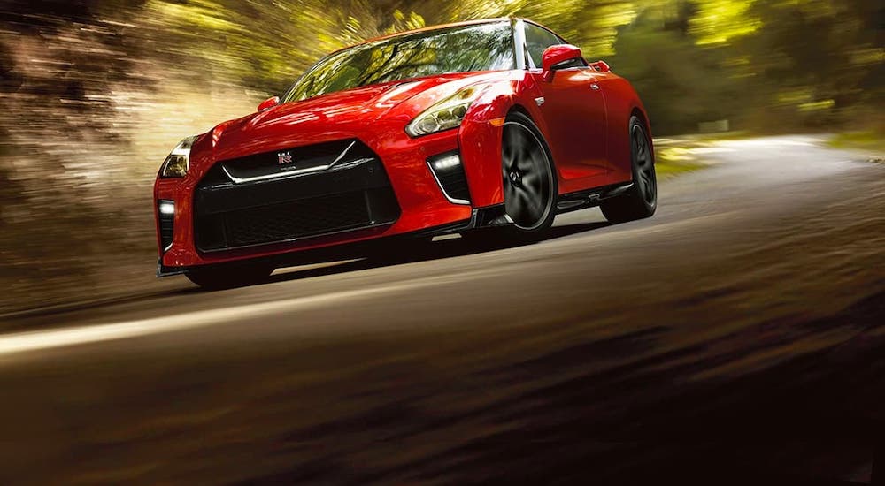 A red 2021 Nissan GT-R is driving on a woodland road.
