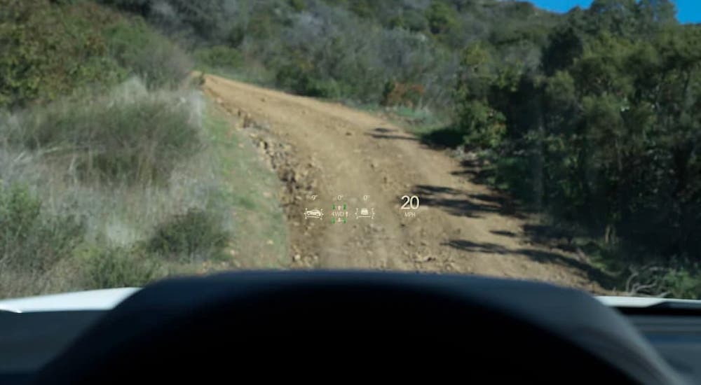 Some newer car tech, a head up display, is shown on a 2021 GMC Yukon from the driver's perspective as the SUV drives on a dirt road.
