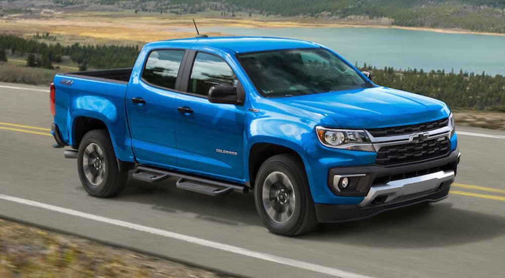 A blue 2021 Chevy Colorado from a Chevy dealer is driving past a lake.