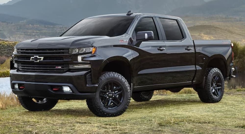 A black 2021 Chevy Silverado is parked on grass in front of a lake.