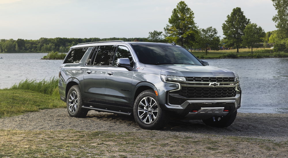 A grey 2021 Chevy Suburban is parked on grass in front of a lake.