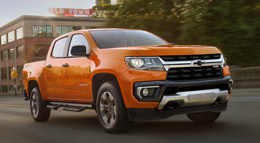 An orange 2021 Chevy Colorado from a Chevy dealer is driving on a city street.