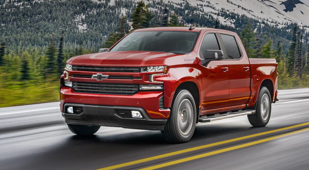 A red 2021 Chevy Silverado 1500 is driving on a road past a mountain.