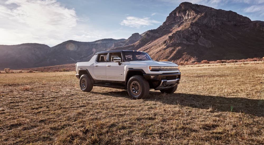 A recent headline in current auto news, a white 2022 GMC Hummer EV, is parked in a field in front of mountains.