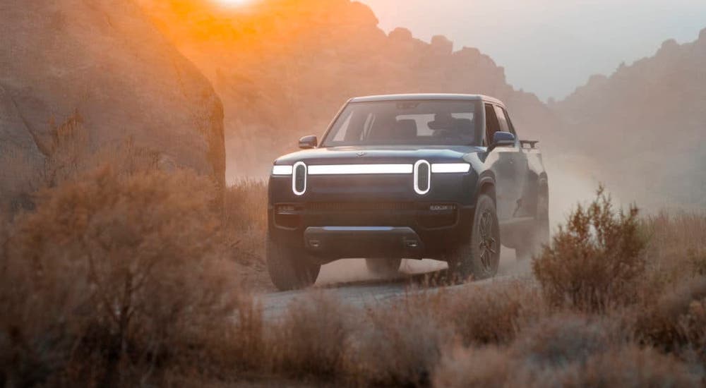 A dark blue Rvian R1T is driving on a dusty trail.