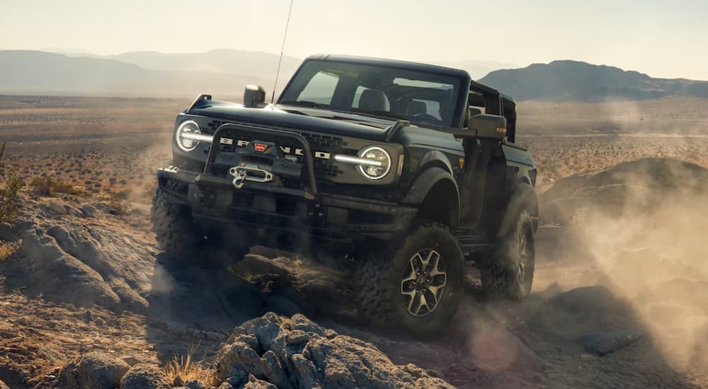 A black 2021 Ford Bronco from a Ford Bronco dealer is on rocks while off-roading in the desert.
