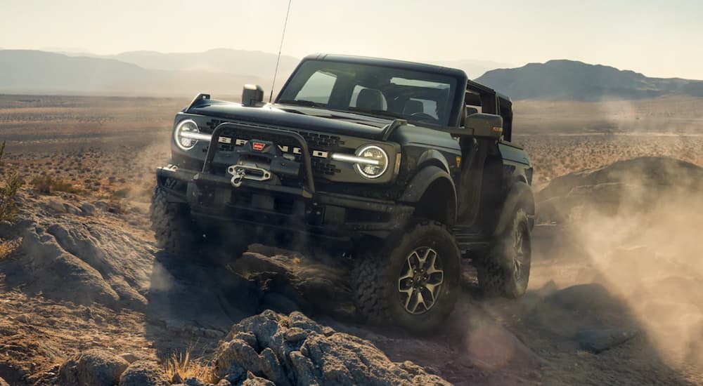 A black 2021 Ford Bronco from a Ford Bronco dealer is on rocks while off-roading in the desert.