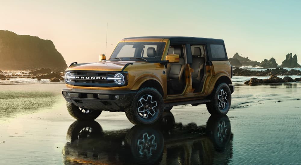 A yellow 2021 Ford Bronco Outer Banks with no doors is parked on a beach.