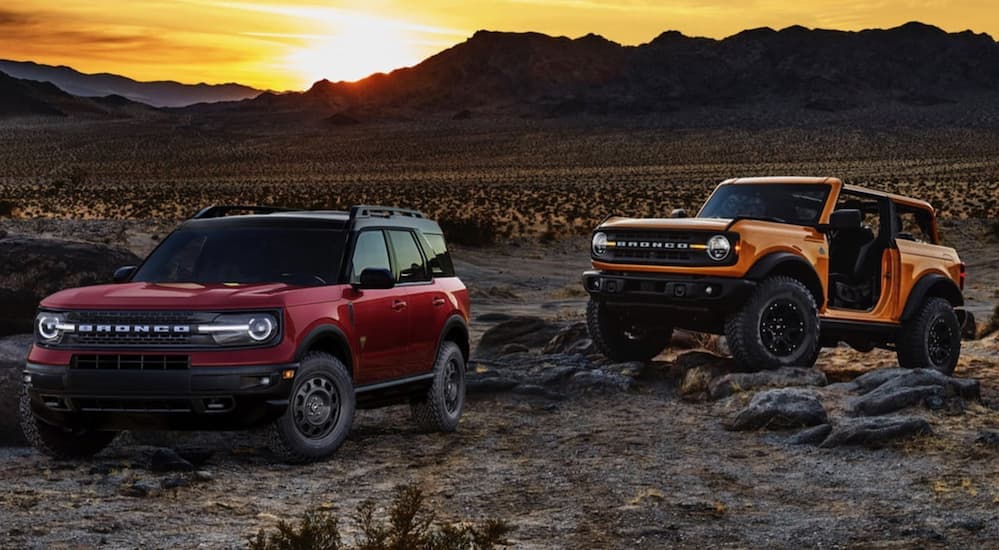 A red 2021 Ford Bronco Sport is parked next to an orange 2021 Bronco 2 Door in the desert at sunset.