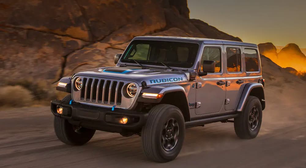 A silver 2021 Jeep Wrangler 4xe is driving past desert rocks after leaving a Jeep dealer.