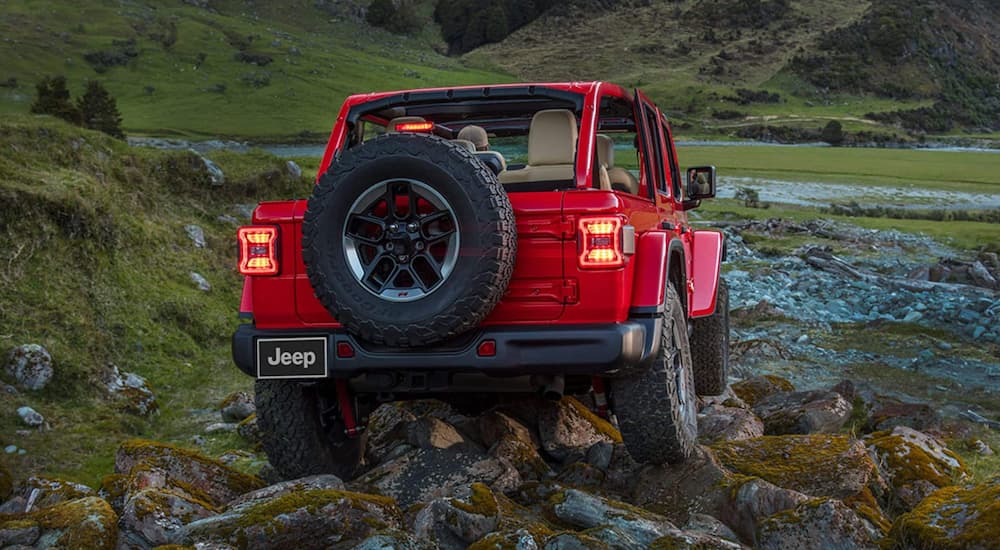 A red 2021 Jeep Wrangler Rubicon is shown from the rear off-roading on rocky terrain.