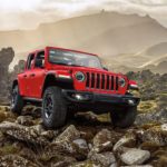 A red 2021 Jeep Wrangler Rubicon Unlimited is off-roading on a rocky mountain trail.