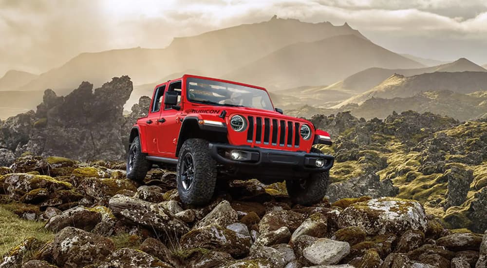 A red 2021 Jeep Wrangler Rubicon Unlimited is off-roading on a rocky mountain trail.