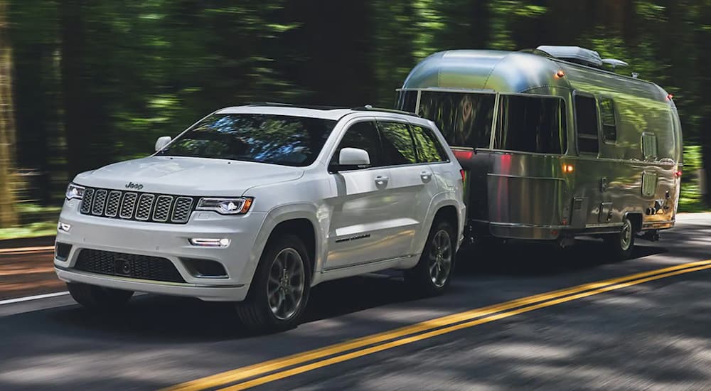 A white 2021 Jeep Grand Cherokee is towing an Airstream on a shady road.