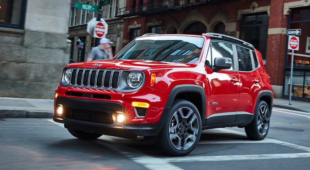 A red 2021 Jeep Renegade from a Jeep dealer is driving around a corner on a city street.