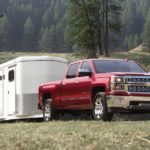 A red 2015 Chevy Silverado 1500 is towing a trailer in a field.