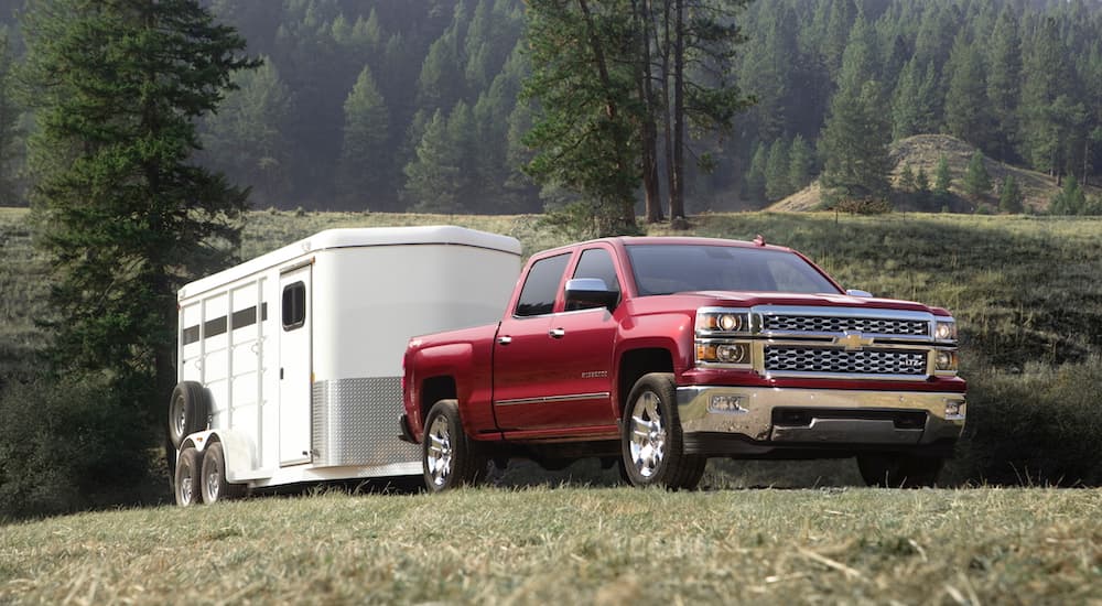 A red 2015 Chevy Silverado 1500 is towing a trailer in a field.