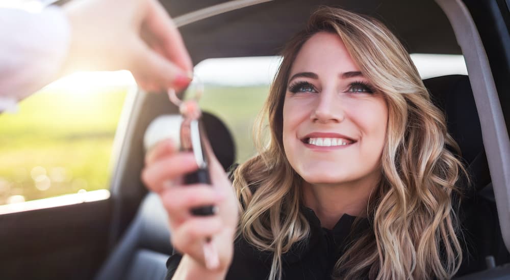 A close up shows a smiling woman being handed a set of car keys.