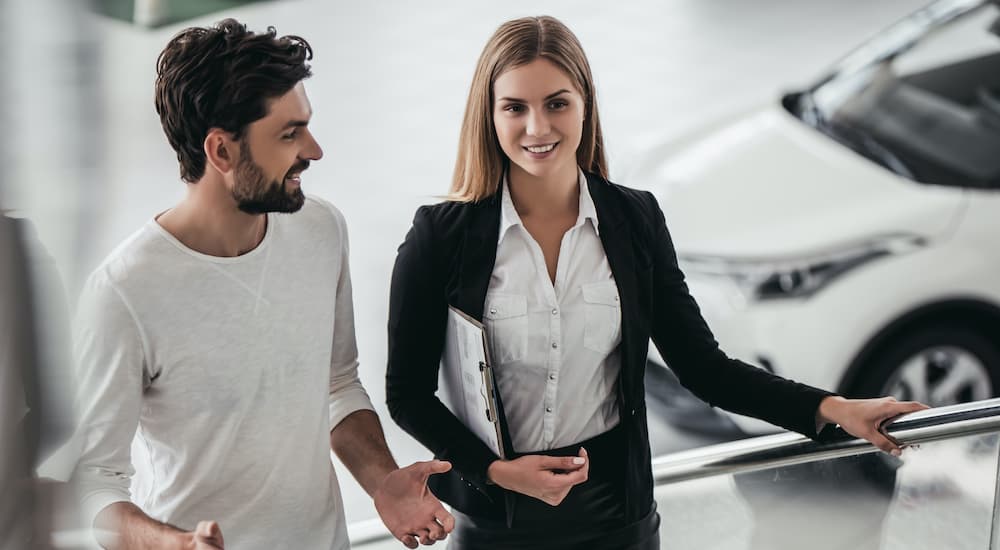 A close up shows a customer and salesperson walking up a set of stairs with a car in the background.