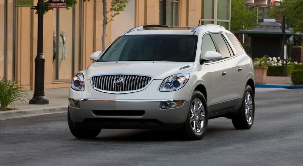 A white 2012 used Buick Enclave is parked in front of a city building.