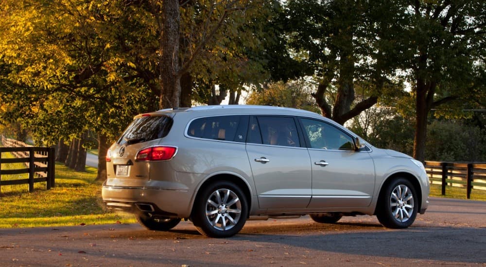 A silver 2014 used Buick Enclave is parked in front of trees at sunset.