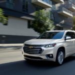 A white 2019 Chevy Traverse is driving on a city street after leaving a used Chevy dealer.