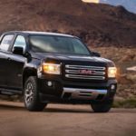 A black 2017 GMC Canyon is parked on a dirt road running between mountains.