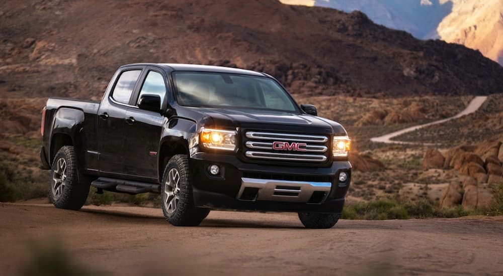 A black 2017 GMC Canyon is parked on a dirt road running between mountains.