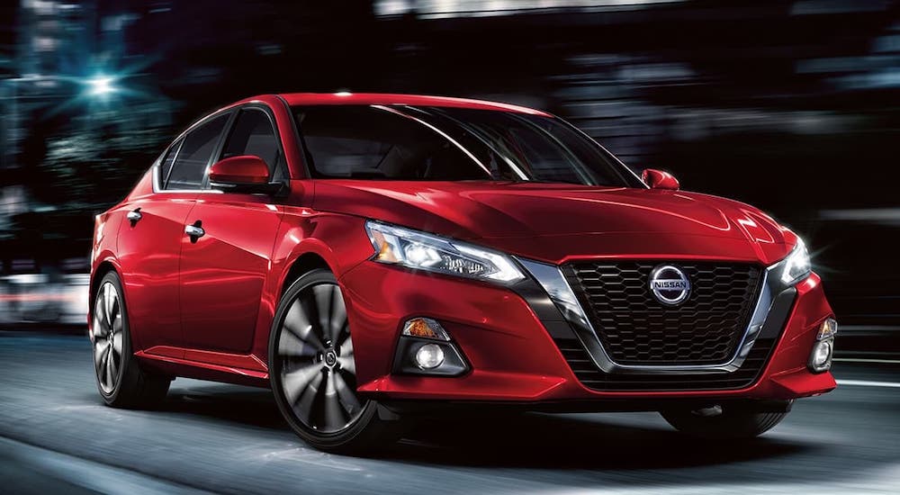 A red 2021 Nissan Altima is driving on a city street at night.