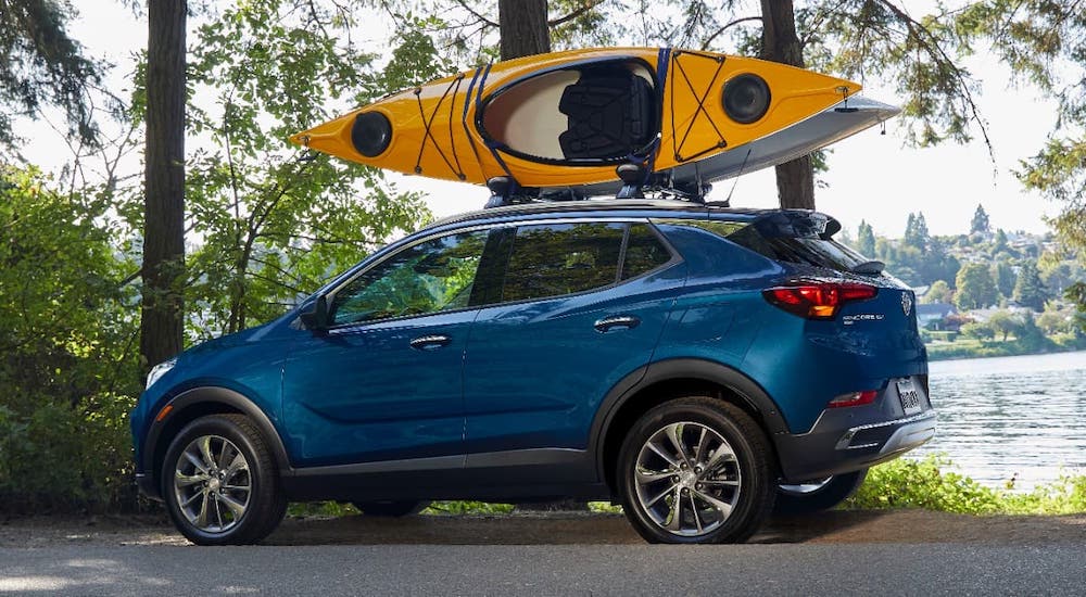 A blue 2021 Buick Encore GX with kayaks on the roof is parked in front of a lake.