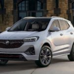 A silver 2021 Buick Encore GX is parked in front of a tan brick building.