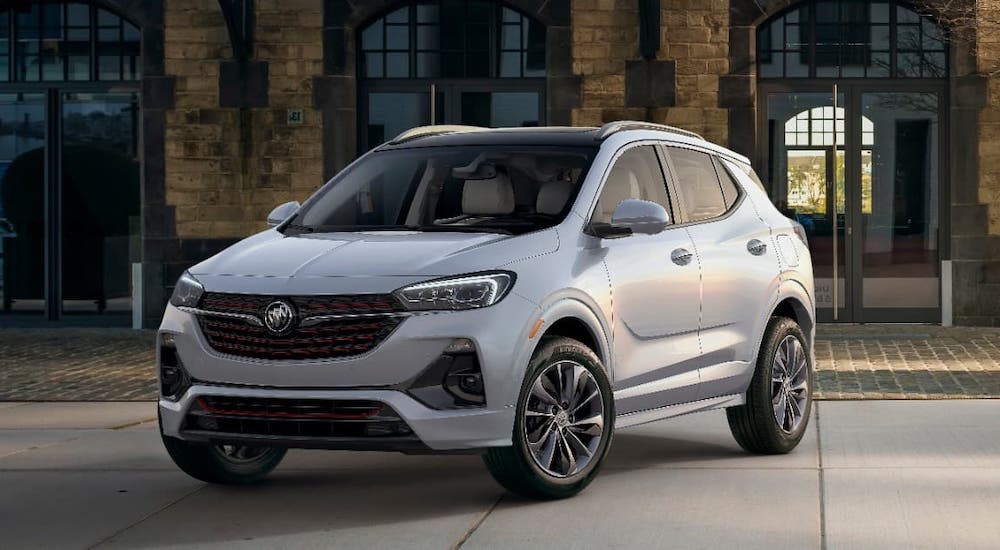 A silver 2021 Buick Encore GX is parked in front of a tan brick building.
