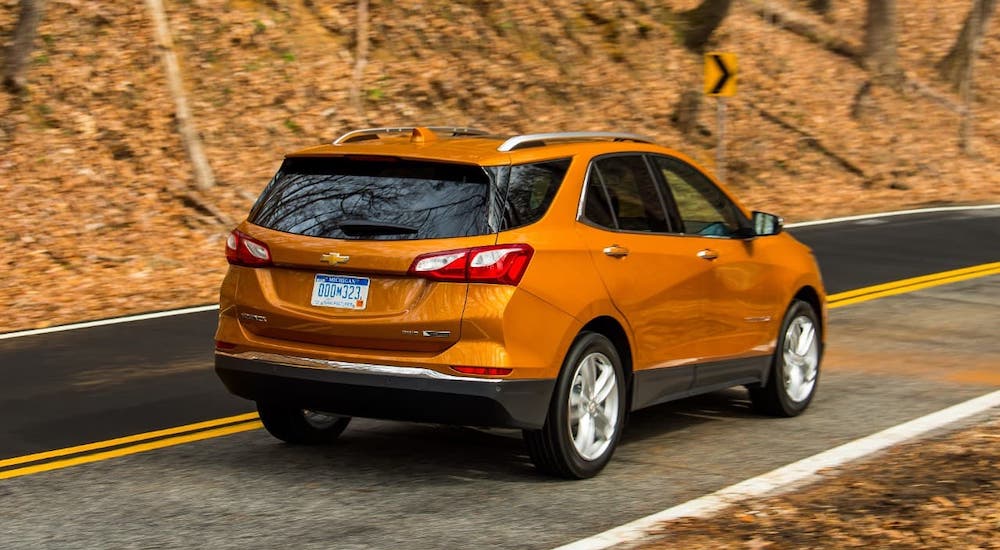 An orange 2021 Chevy Equinox is driving away on a road with fall foliage.